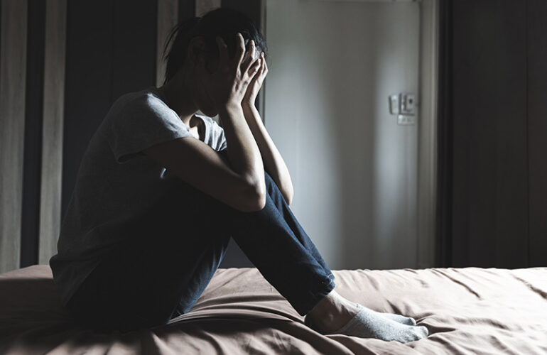 A woman sits in the darkness and covers her face while coping with grief in recovery.