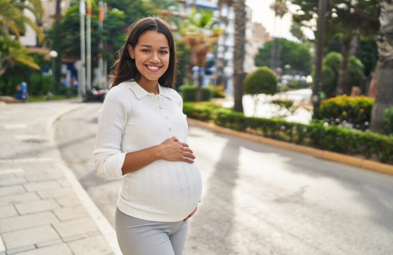 A pregnant woman smiles while walking outside to improve her mental health during pregnancy.