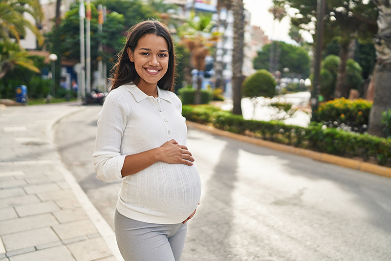 A pregnant woman smiles while walking outside to improve her mental health during pregnancy.